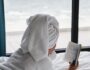 Lonely female with a white robe and a towel lying down in the bed and reading a book near the window
