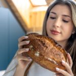 Woman examines fresh homemade bread in kitchen. Bread aroma.