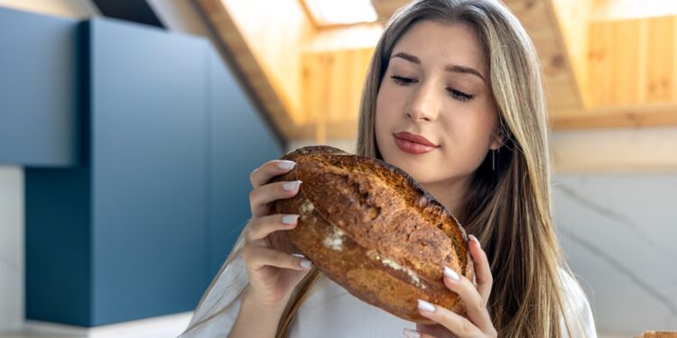 Woman examines fresh homemade bread in kitchen. Bread aroma.