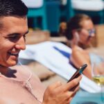 Cheerful man in headphones using a smartphone, lying on a lounger