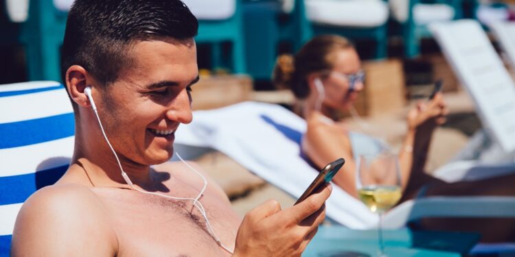 Cheerful man in headphones using a smartphone, lying on a lounger