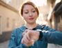 Young redhead woman wearing sportswear listening to music looking stopwatch at street